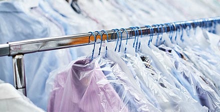 At Excellent Dry Cleaners, a clothes rack holding several shirts protected by transparent plastic covers stands prominently. The shirts hang neatly on blue hangers, and the image focuses on the pristine row of garments.